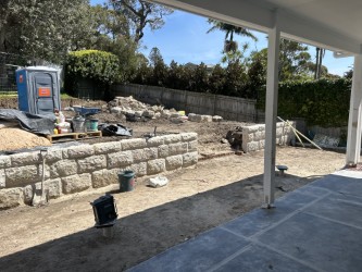 Sandstone block retaining wall under construction with bare yard